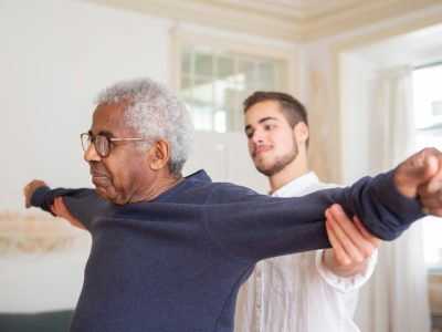 pexels-photo-7551627-7551627 A senior man is assisted by a caregiver for stretching exercises indoors.